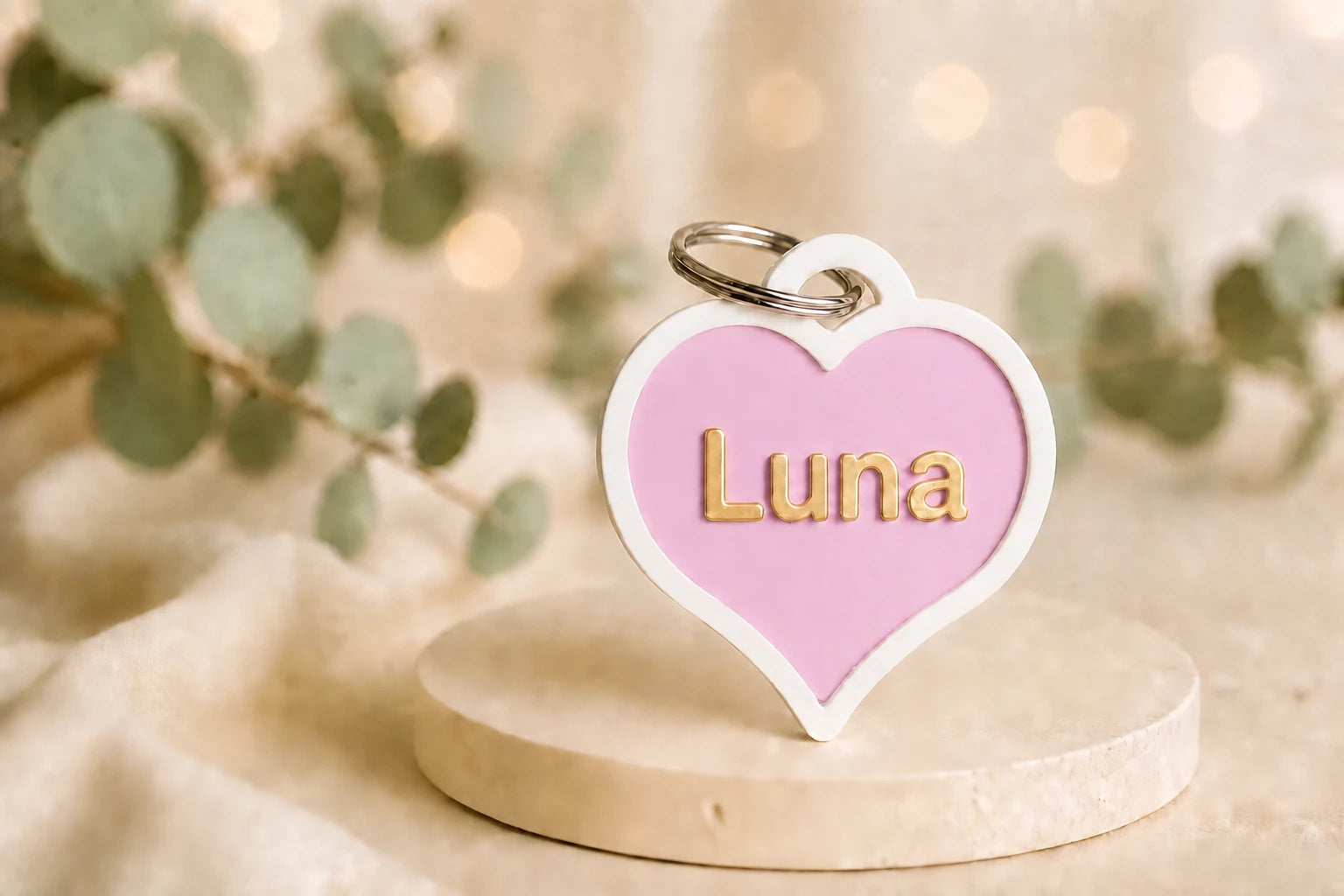 Pink-weiße Herzmarke Herzenshund mit goldfarbenem Namen Luna auf einem hellen Steinpodest